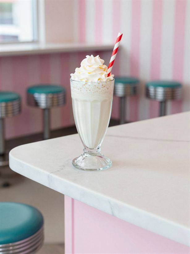 A thick milkshake with whipped cream and a striped straw on the counter.